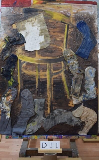 Assemblageartige Collage mit einem runden Tisch, Textblatt, Stoff- und Sockenformen in Braun, Blau und Grau.